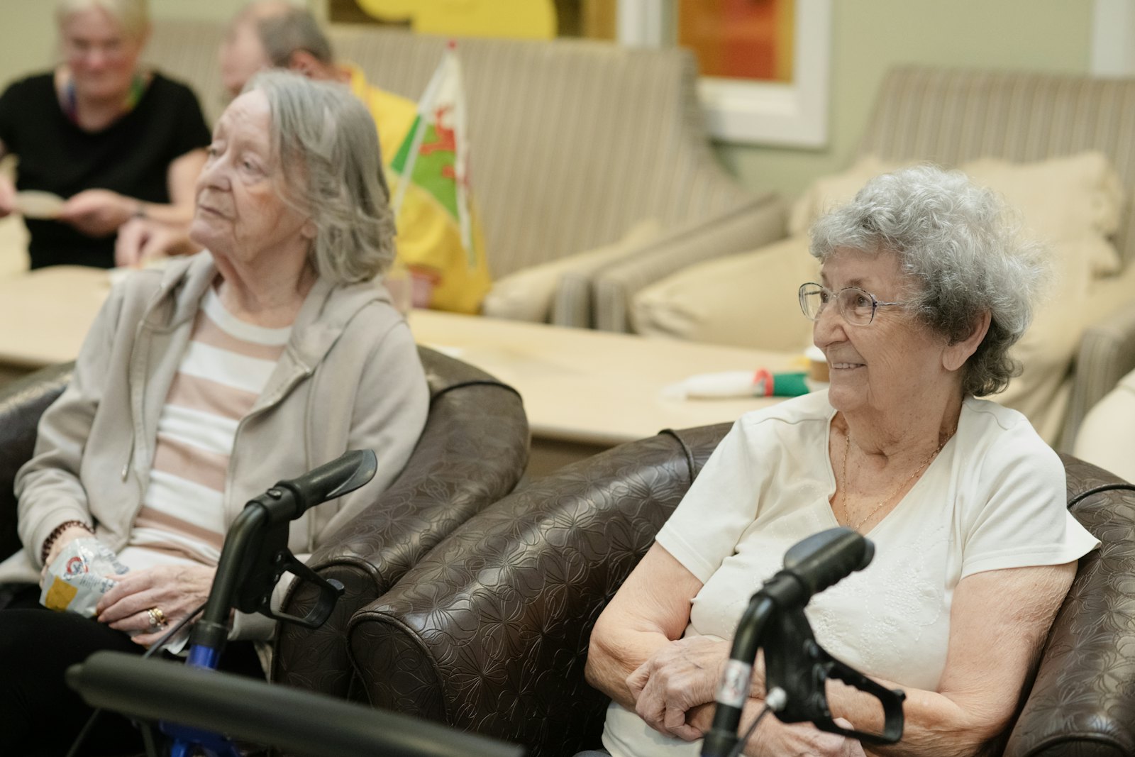 Two residents sitting in armchairs in the lounge of a senior living community.